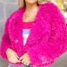 Close up view of model wearing the Make A Statement Jacket which features hot pink soft shag fabric, hidden button closures, two front pockets, cropped waist and long balloon sleeves. The jacket is open. 