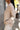 Side view of model wearing the Fireside Feels Sweater in Beige which features beige fabric, a high-low hemline, one pocket on the left chest, a round neckline, and long sleeves.