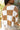 Back view of model wearing the Check This Out Sweater which features white and camel knit fabric with a checkered pattern, a round neckline, a cropped waist and long sleeves.