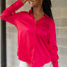 Close up view of model wearing the Up All Night Satin Top which features hot pink satin fabric, monochromatic button up, collared neckline, high-low hem and long sleeves with button closure cuffs.
