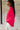 Side view of model wearing the Up All Night Satin Top which features hot pink satin fabric, monochromatic button up, collared neckline, high-low hem and long sleeves with button closure cuffs.