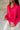 Close up side view of model wearing the Up All Night Satin Top which features hot pink satin fabric, monochromatic button up, collared neckline, high-low hem and long sleeves with button closure cuffs.