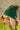 Front view of model wearing the Anchorage Beanie in Green, that has forest green knit fabric with a stitched pattern, a front patch that says "C.C exclusives", and a brown faux-fur pompom.