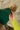 Close-up side view of model wearing the Anchorage Beanie in Green, that has forest green knit fabric with a stitched pattern, a front patch that says "C.C exclusives", and a brown faux-fur pompom.