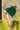 Side view of model wearing the Anchorage Beanie in Green, that has forest green knit fabric with a stitched pattern, a front patch that says "C.C exclusives", and a brown faux-fur pompom.