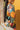 Side view of model wearing the Better Believe It Top which features orange, teal, maroon and white fabric with a floral pattern, a button-up front with wooden buttons, a collared neckline, and long sleeves with elastic wrists.