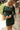 Close up view of model wearing the Unforgettable Dress which features green sheen fabric, smalls slits on each side of the hem, ruching on the sides, round neckline, lining and long sleeves.