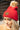 Side view of model wearing the Anchorage Beanie in Red, that has red knit fabric with a stitched pattern, a front patch that says "C.C exclusives", and a brown faux-fur pompom.
