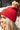 Side view of model wearing the Anchorage Beanie in Red, that has red knit fabric with a stitched pattern, a front patch that says "C.C exclusives", and a brown faux-fur pompom.

