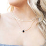 Close up view of model wearing the Date Night Necklace which features double layer gold linked chain and flat layer with a black stone.