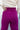 Close upper back view of model wearing the Be Fearless Pants, that have magenta corduroy fabric, two front pockets, a paperbag waist with a tie, a zipper and button closure, and straight legs