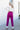 Full body back view of model wearing the Be Fearless Pants, that have magenta corduroy fabric, two front pockets, a paperbag waist with a tie, a zipper and button closure, and straight legs
