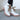 Close-up side view of model wearing the  Brighton Lace-Up Boot, that has an off white faux-leather and nylon upper, a taupe rubber sole with a 3" heel, and cognac laces.