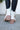 Close-up back view of model wearing the  Brighton Lace-Up Boot, that has an off white faux-leather and nylon upper, a taupe rubber sole with a 3" heel, and cognac laces.