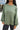 Close up view of model wearing the This Is Easy Top in Olive which features green fabric, hem detailing, a high-low hem with slits, a round neckline, and dropped shoulder balloon long sleeves.