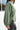 Side view of model wearing the This Is Easy Top in Olive which features green fabric, hem detailing, a high-low hem with slits, a round neckline, and dropped shoulder balloon long sleeves.