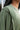 Close up side view of model wearing the This Is Easy Top in Olive which features green fabric, hem detailing, a high-low hem with slits, a round neckline, and dropped shoulder balloon long sleeves.