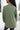 Close up back view of model wearing the This Is Easy Top in Olive which features green fabric, hem detailing, a high-low hem with slits, a round neckline, and dropped shoulder balloon long sleeves.