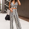 Full body front view of model wearing the Going Rogue Top, which an ivory and black geometric print with a slight sheen, a deep V surplice neck, a thick straps, a cropped fit, and a side zipper closure. Worn with matching pants.