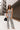 Full body front view of model wearing the Going Rogue Top, which an ivory and black geometric print with a slight sheen, a deep V surplice neck, a thick straps, a cropped fit, and a side zipper closure. Worn with matching pants.