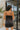 Back view of the City Walk Dress that features a black silky material, a cowl neckline, a sleeveless design with thin adjustable straps, a tie at the waist, a draped design, a back zipper closure, and a mini length.