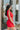 Side view of the Speechless Romper that features a red chiffon material, a surplice neckline, a short sleeve with a slit, a waist tie detail, a faux wrap skirt overlay, a shorts back, and a back zipper closure.