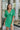Frontal view of the Speechless Romper that features a green chiffon material, a surplice neckline, a short sleeve with a slit, a waist tie detail, a faux wrap skirt overlay, a shorts back, and a back zipper closure.