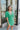 Frontal view of the Speechless Romper that features a green chiffon material, a surplice neckline, a short sleeve with a slit, a waist tie detail, a faux wrap skirt overlay, a shorts back, and a back zipper closure.
