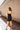Full body back view of model wearing the Show Stopper Dress in Black, which features a black chiffon material, a straight neckline, a sleeveless design with thin straps, and a ruched overlapped detail on the skirt