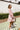 Side view of model wearing the Lost In A Daydream Dress, which features a blush colored material, a white and orange floral print, a V neckline, a long sheer sleeve with smocked detailing at the wrist, a ruffle detail at the bottom
