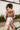 Back
view of model wearing the Lost In A Daydream Dress, which features a blush colored material, a white and orange floral print, a V neckline, a long sheer sleeve with smocked detailing at the wrist, a ruffle detail at the bottom