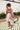 Back view of model wearing the Lost In A Daydream Dress, which features a blush colored material, a white and orange floral print, a V neckline, a long sheer sleeve with smocked detailing at the wrist, a ruffle detail at the bottom