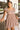 Front view of model wearing the Happy And Free Babydoll Dress, which has a brown gingham print, a straight neckline, a short puffy sleeve with, a parachute bottom, an elastic bottom hem, and a back zipper closure.