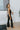 Side view of model wearing the Daily Ritual Faded Jeans, which have a stretchy denim material, a faded black wash, a flare leg fit, a high-rise waist, a five button closure, two front pockets, a frayed/distressed flare hem, and two back pockets