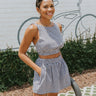 Close-up front view of model wearing the Kennedy Gingham Top that has a black and white gingham print, a round neckline, a sleeveless design with thick straps, an elastic bottom hem, a cropped fit, and an open back. Worn with matching skort.