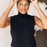 Frontal view of the Meet Me In Maine Sweater Tank that features a black stretchy knit material, a turtleneck, a sleeveless design, and a thick bottom hem.