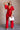 Full body view of model wearing the Jessica Red Plunge Neckline Jumpsuit which features red knit fabric, a plunge neckline, short flare sleeves, an open back, a monochrome back zipper with a hook closure, and flare pant legs.