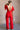 Full body back view of model wearing the Jessica Red Plunge Neckline Jumpsuit which features red knit fabric, a plunge neckline, short flare sleeves, an open back, a monochrome back zipper with a hook closure, and flare pant legs.