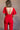 Back view of model wearing the Jessica Red Plunge Neckline Jumpsuit which features red knit fabric, a plunge neckline, short flare sleeves, an open back, a monochrome back zipper with a hook closure, and flare pant legs.