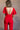 Back view of model wearing the Jessica Red Plunge Neckline Jumpsuit which features red knit fabric, a plunge neckline, short flare sleeves, an open back, a monochrome back zipper with a hook closure, and flare pant legs.