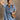 front view of model wearing the Aubrie Washed Blue Short Sleeve Mini Dress that has washed light blue chambray fabric, a chest pocket, a hidden quarter button-up, a v neck, a collar, a frayed hem, and cuffed short sleeves.