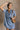 front view of model wearing the Aubrie Washed Blue Short Sleeve Mini Dress that has washed light blue chambray fabric, a chest pocket, a hidden quarter button-up, a v neck, a collar, a frayed hem, and cuffed short sleeves.