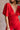 Close up front view of model wearing the Jessica Red Plunge Neckline Jumpsuit which features red knit fabric, a plunge neckline, short flare sleeves, an open back, a monochrome back zipper with a hook closure, and flare pant legs.