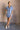 Full body front view of model wearing the Aubrie Washed Blue Short Sleeve Mini Dress that has washed light blue chambray fabric, a chest pocket, a hidden quarter button-up, a v neck, a collar, a frayed hem, and cuffed short sleeves.