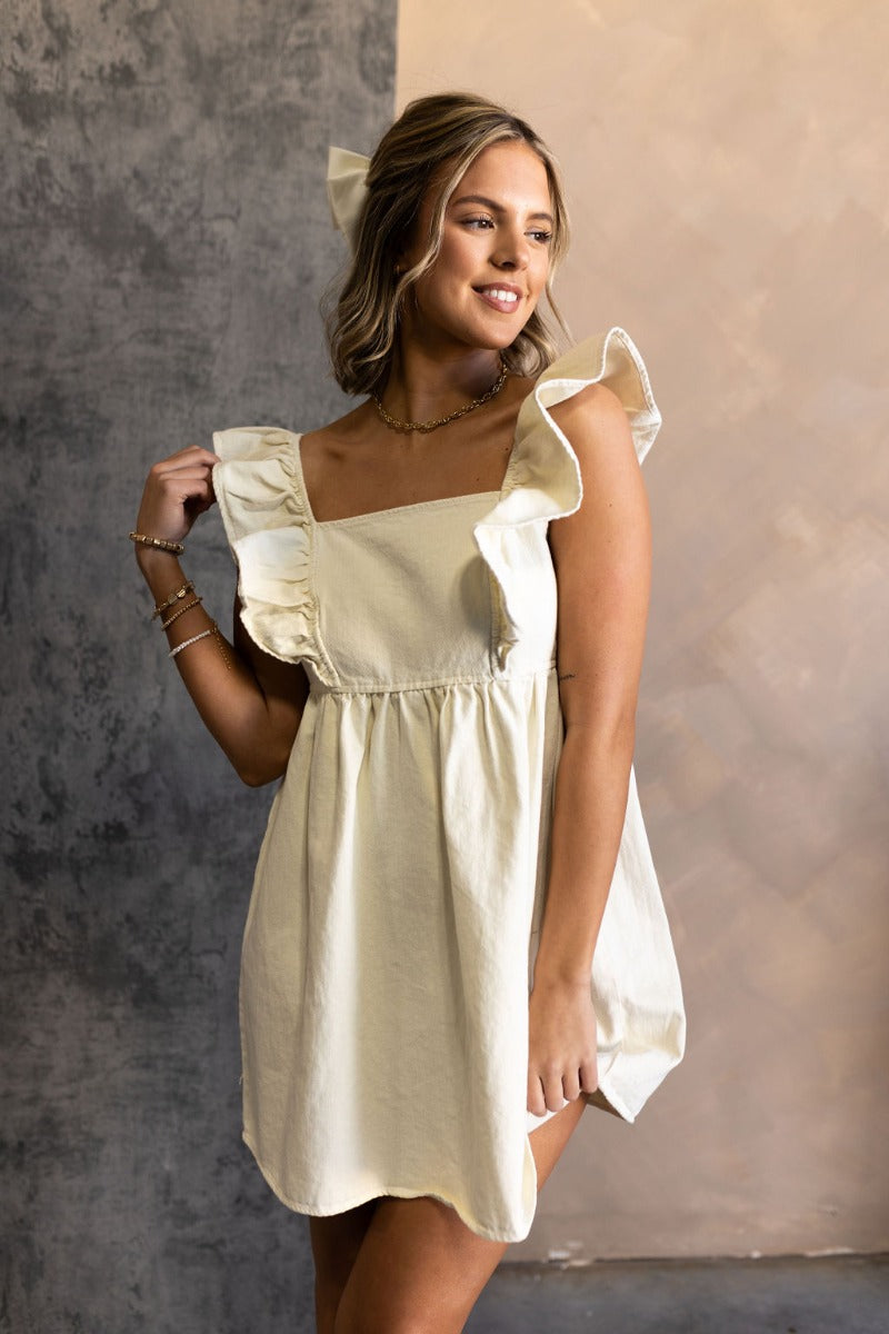 front view of model wearing the Rory Cream Ruffle Sleeveless Mini Dress that features cream cotton denim fabric, mini length, a square neckline, ruffle straps, and a smocked back.