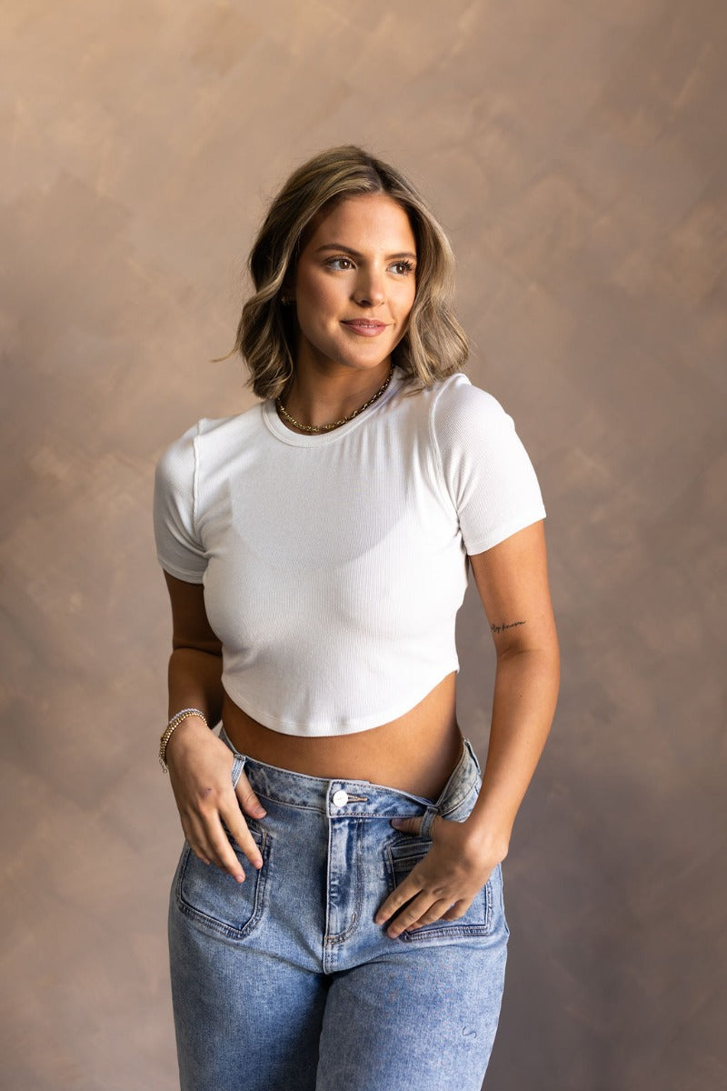 Front view of model wearing the Gabrielle White Short Sleeve Crop Top that have white ribbed knit fabric, a cropped waist, a round neckline and short sleeves.
