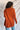 Back view of model wearing the Above All Else Sweater, which features rust-colored knit fabric with a front chest pocket, a round neckline, long sleeves, and side slits.