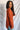 Side view of model wearing the Above All Else Sweater, which features rust-colored knit fabric with a front chest pocket, a round neckline, long sleeves, and side slits.