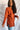 Side view of model wearing the Above All Else Sweater, which features rust-colored knit fabric with a front chest pocket, a round neckline, long sleeves, and side slits.