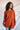 Front view of model wearing the Above All Else Sweater, which features rust-colored knit fabric with a front chest pocket, a round neckline, long sleeves, and side slits.